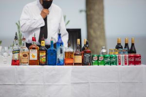 A man standing behind a wedding table full of liquor bottles.