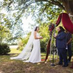 A wedding ceremony with the bride and groom exchanging vows under a tree.