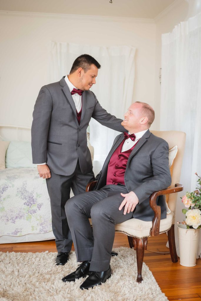 Two men in suits candidly preparing for a wedding in a room.