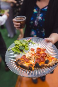 A woman is holding a pizza on a plate with wedding details.
