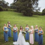A wedding portrait of bridesmaids in blue dresses in a field.