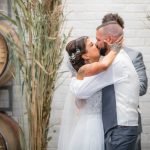 A bride and groom kiss during their wedding ceremony in front of barrels.