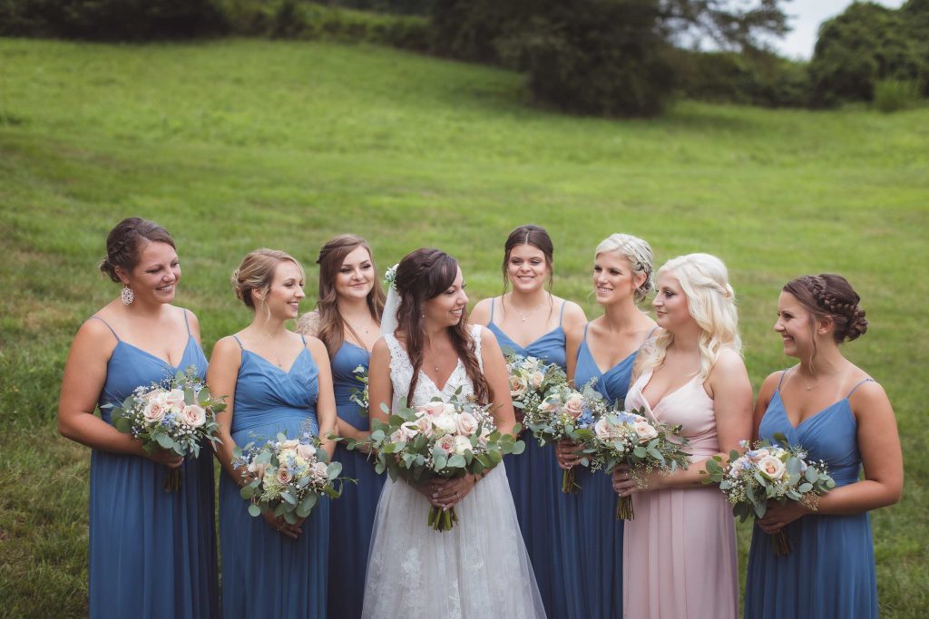 A wedding portrait of bridesmaids in blue dresses in a field.