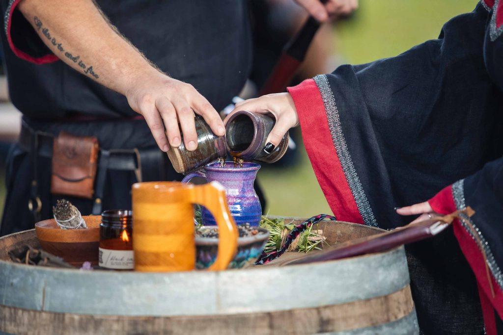A person performing a ceremonial pouring of a drink out of a barrel at a wedding.