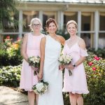 Three bridesmaids in pink dresses posing for a wedding portrait in front of a house.