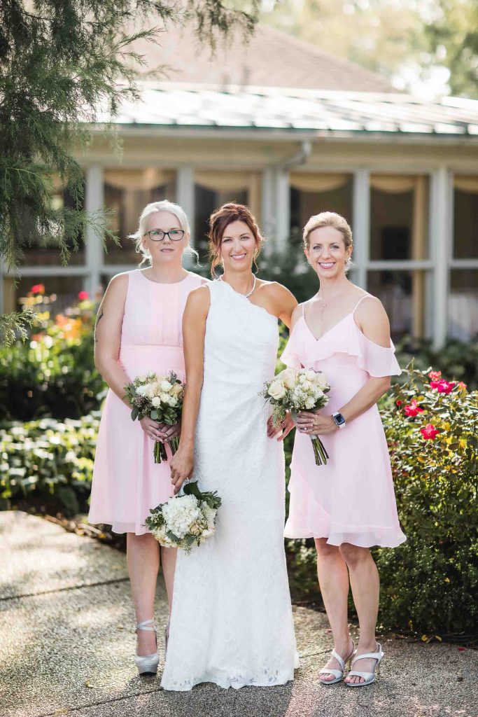 Three bridesmaids in pink dresses posing for a wedding portrait in front of a house.