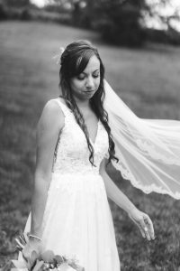 Black and white portrait of a bride holding her veil at her wedding.