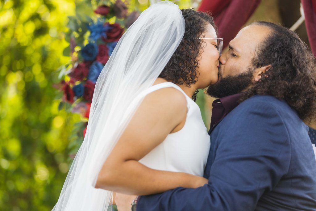 A couple exchanging vows during their wedding ceremony under an arbor.
