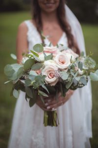 A bride showcasing wedding details with a bouquet of roses and eucalyptus.