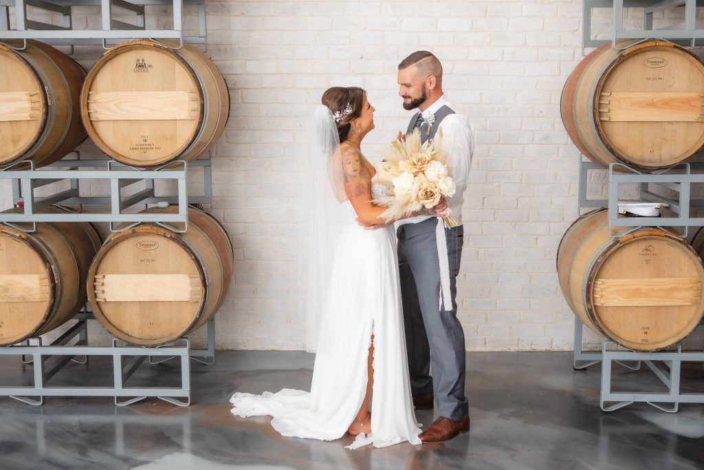 A wedding portrait featuring a bride and groom in front of wine barrels.