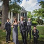 A group of groomsmen posing in front of a mansion for a wedding portrait.