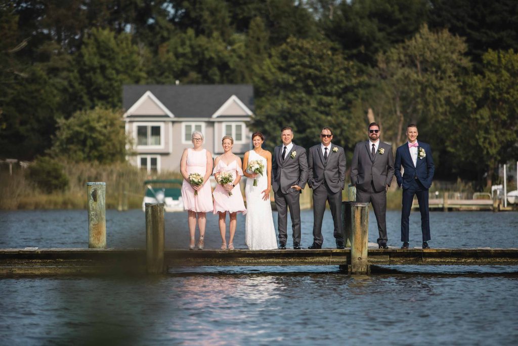 A group of bridesmaids and groomsmen posing for a wedding portrait on a dock.