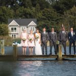 A group of bridesmaids and groomsmen posing for a wedding portrait on a dock.