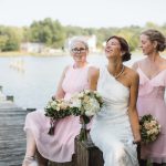 A bride and her bridesmaids pose for a wedding portrait on a dock.
