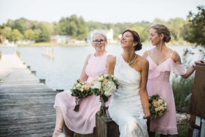 A bride and her bridesmaids pose for a wedding portrait on a dock.