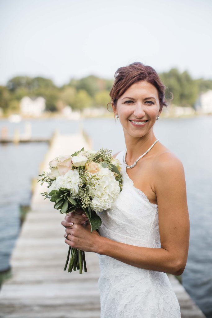 A wedding portrait of a bride holding her bouquet on a dock.