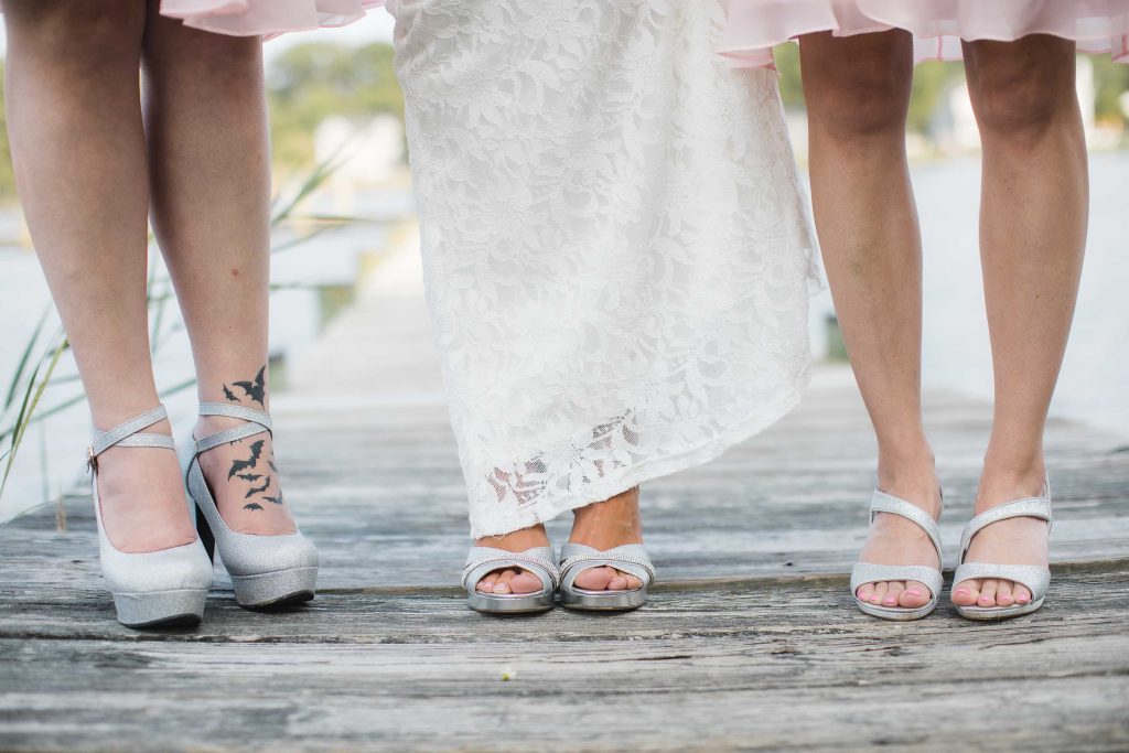 Three bridesmaids showcasing wedding details on a dock with their shoes on.