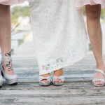 Three bridesmaids showcasing wedding details on a dock with their shoes on.