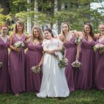 A bride and her bridesmaids pose for a wedding portrait in front of a house.