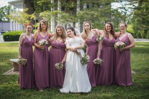 A bride and her bridesmaids pose for a wedding portrait in front of a house.