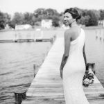 A bride in a white dress poses for her wedding portrait on a dock.