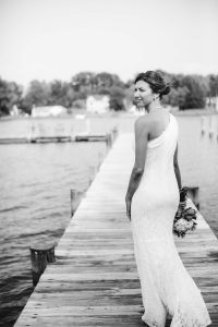A bride in a white dress poses for her wedding portrait on a dock.