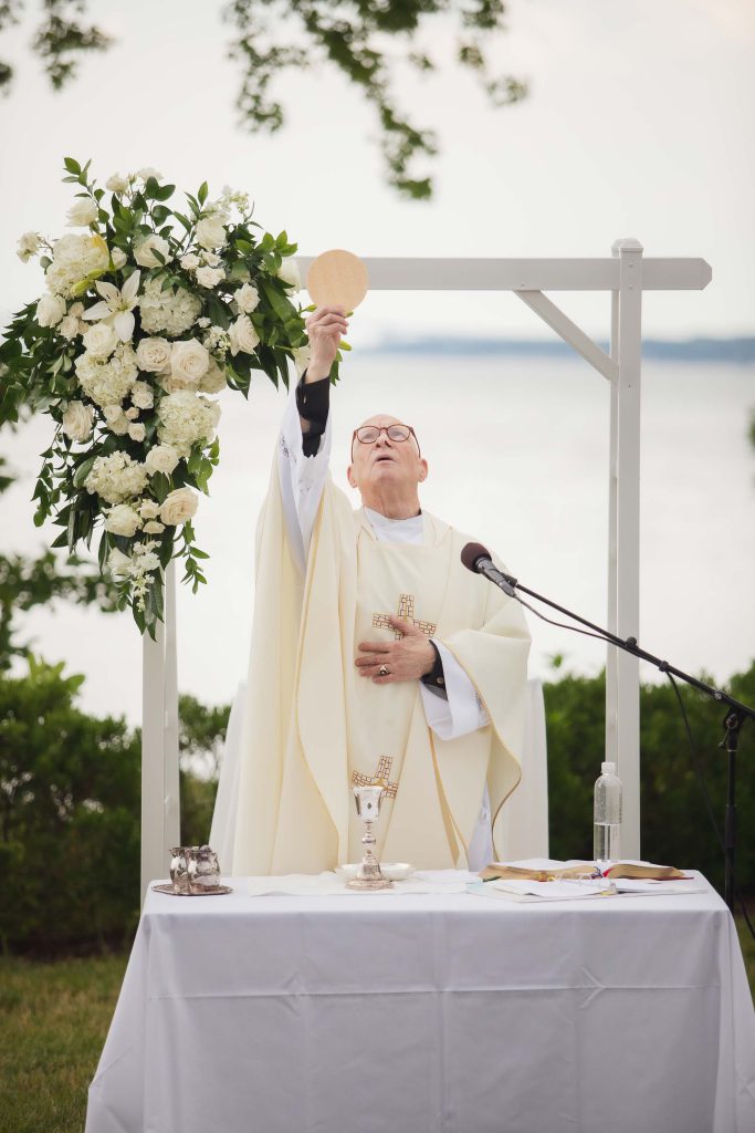 A priest is holding a chalice in front of a group of people during a ceremony.