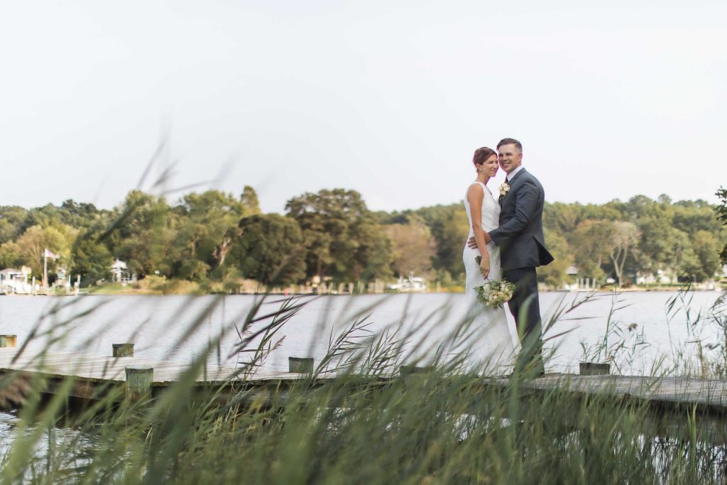 A wedding portrait of a bride and groom on a dock near a lake.