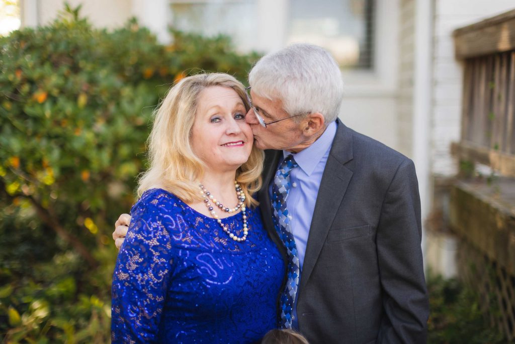 An older couple posing for a wedding portrait in front of a house.
