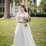 A wedding portrait of a bride in a white wedding dress standing in front of a mansion.