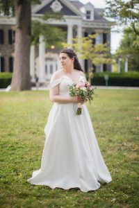 A wedding portrait of a bride in a white wedding dress standing in front of a mansion.