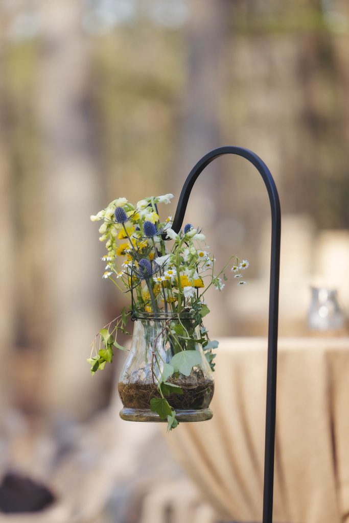 A detailed wedding centerpiece: a vase filled with flowers on a table in a wooded area.