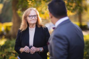 A woman in glasses is candidly talking to a man in a suit during wedding preparation.