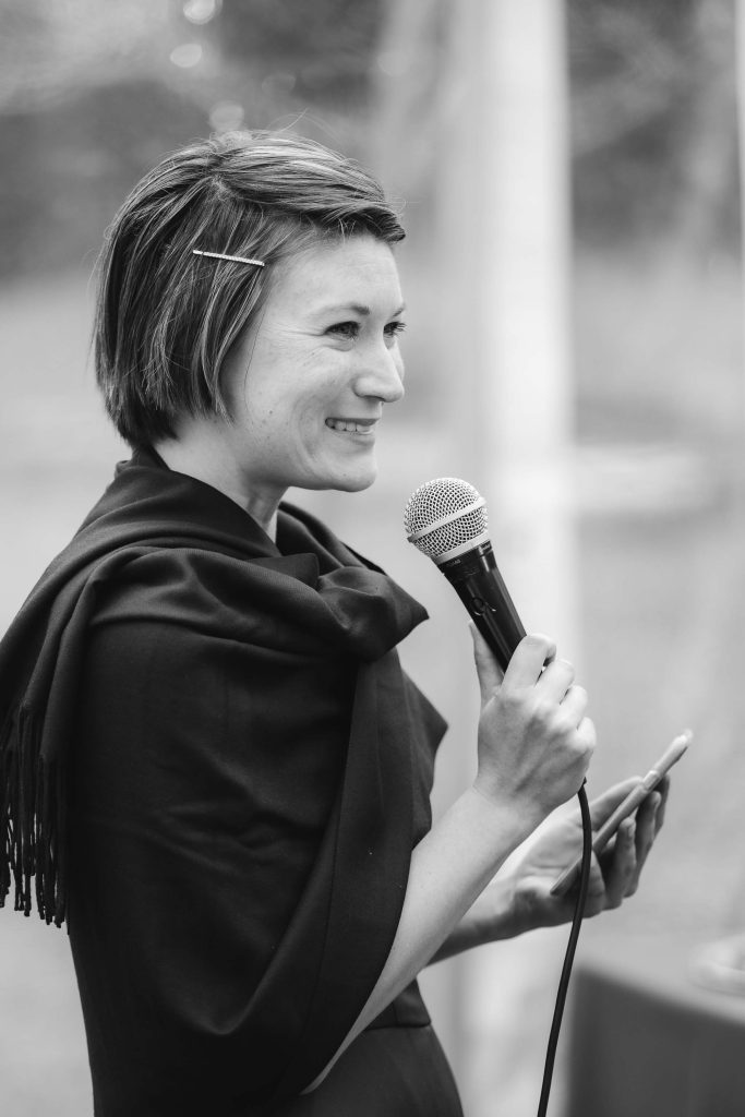 Black and white photo of a woman holding a microphone at a wedding reception.