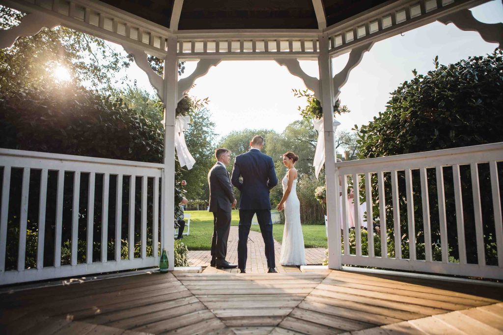 A bride and groom standing in front of a gazebo during their wedding ceremony.