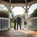 A bride and groom standing in front of a gazebo during their wedding ceremony.