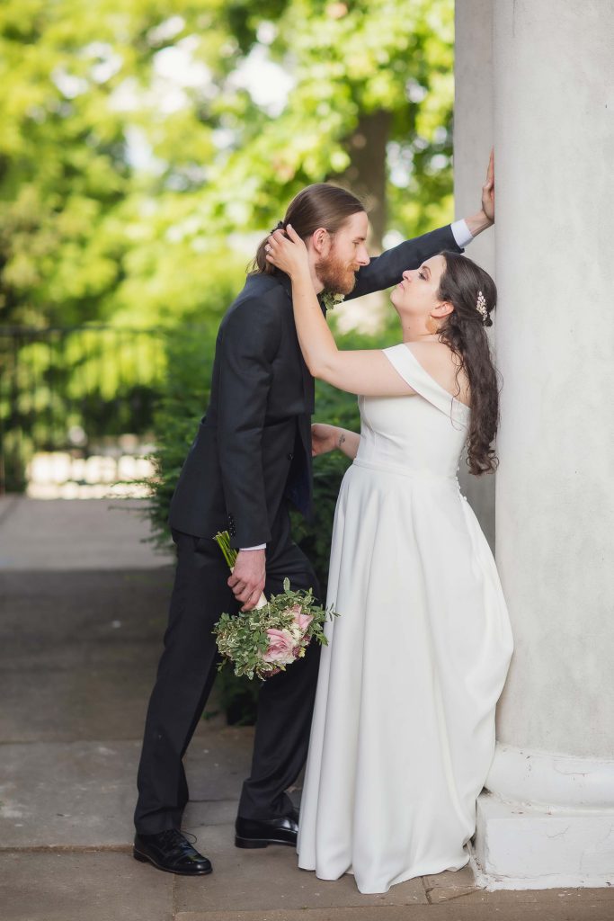 A wedding couple kissing in front of columns.