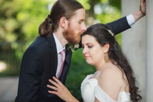 A wedding couple embracing for a portrait in front of a column.