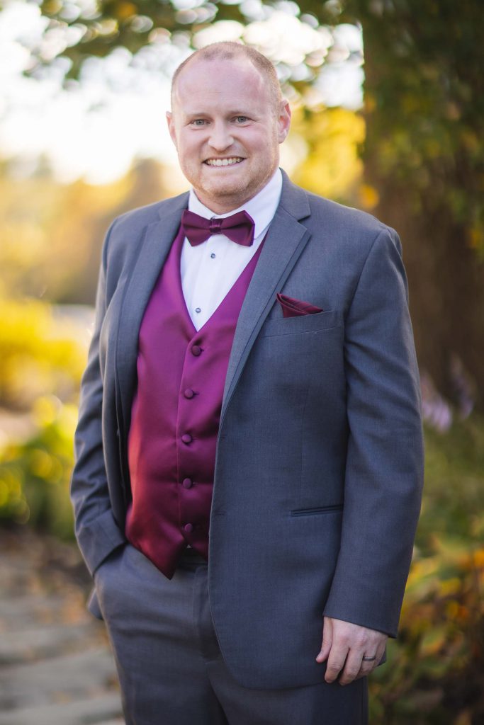 Wedding groom in a gray suit with a purple bow tie.
