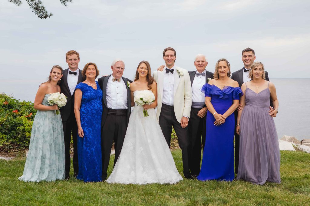 A wedding party poses for a portrait in front of the ocean.