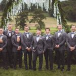 Groomsmen in gray tuxedos standing in front of a wedding arch.