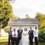 A wedding portrait of bridesmaids and groomsmen posing in front of a house.
