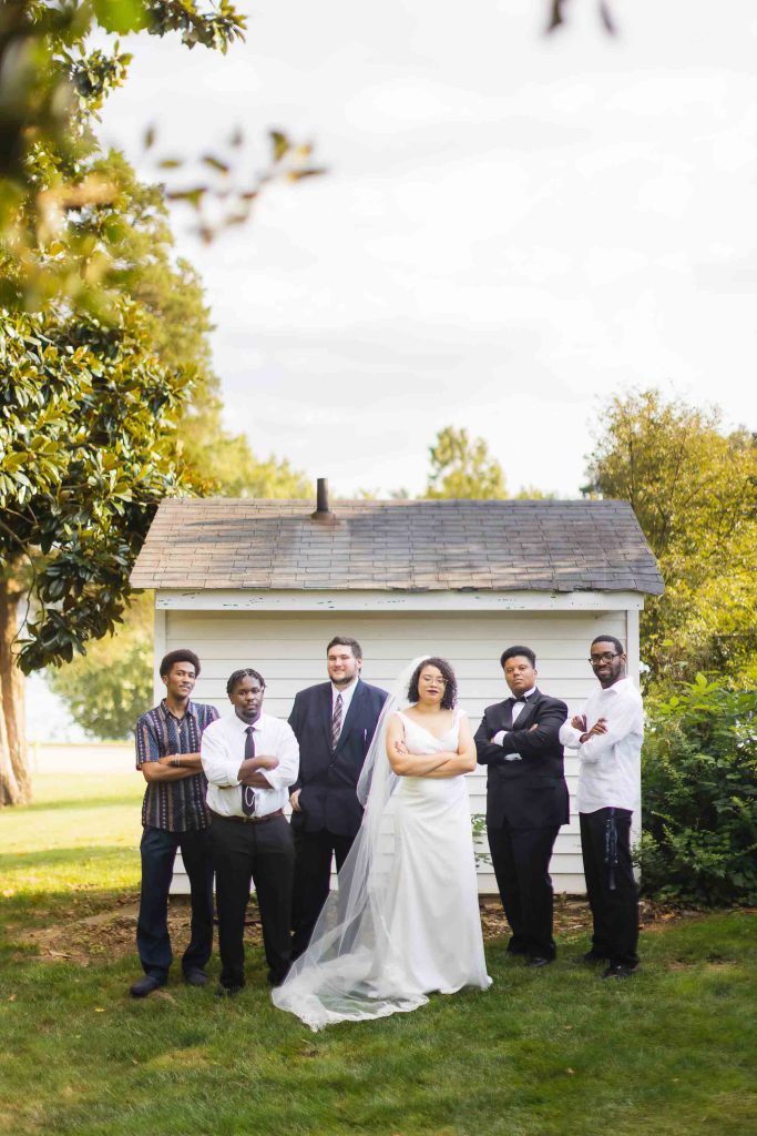 A wedding portrait of bridesmaids and groomsmen posing in front of a house.
