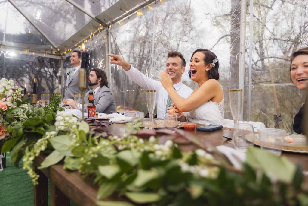 A bride and groom at their wedding reception sitting at a table in a tent.