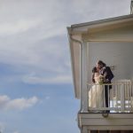 A wedding portrait of a bride and groom kissing on the porch of a house.