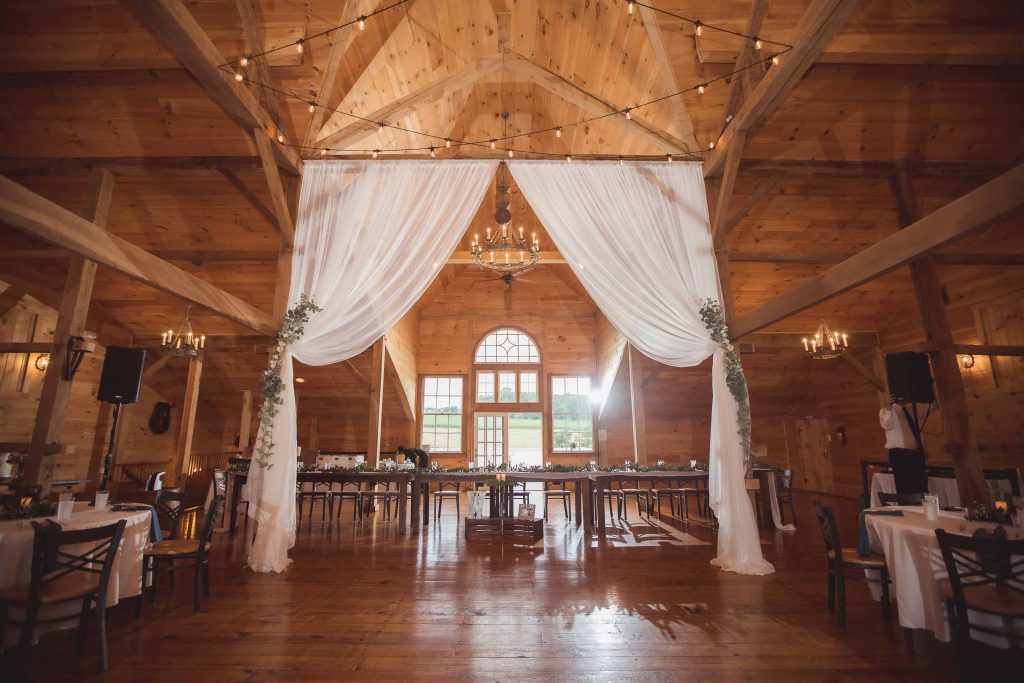 A detailed wedding reception in a barn with white drapes and chandeliers.