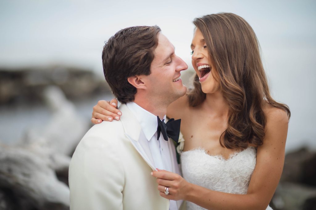 A wedding couple laughing in front of the ocean.