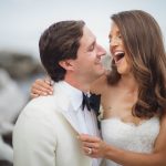 A wedding couple laughing in front of the ocean.