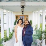A wedding portrait of a bride and groom standing under a covered porch.