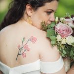 A wedding portrait of a bride with a tattoo on her back holding a bouquet.